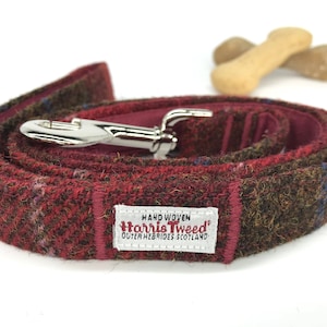 May include: A red, brown, and blue tweed dog leash with a silver clasp. The leash has a label that reads "Hand Woven Harris Tweed Outer Hebrides Scotland".