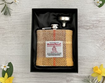 May include: A stainless steel flask with a funnel, wrapped in Harris Tweed fabric. The fabric is a yellow and brown plaid with red accents. The flask is in a black box with a black satin lining.