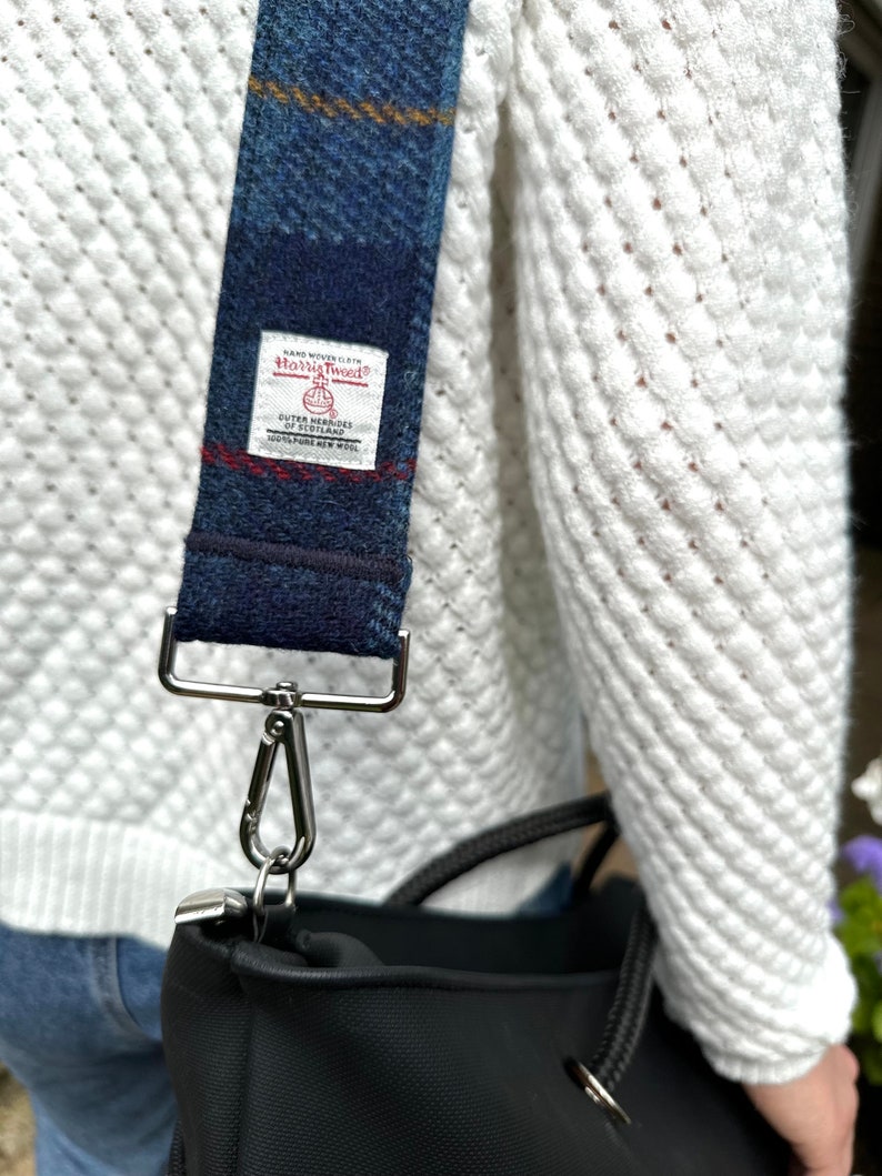 Puede incluir: Un bolso tote negro con una correa de cuadros azules y blancos. La correa tiene una etiqueta que dice "Hand Woven Cloth Harris Tweed Outer Hebrides Scotland 100% Pure New Wool".