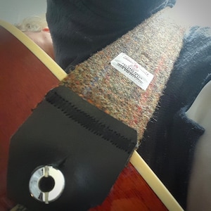 May include: A brown and black guitar strap with a tweed pattern and a white label that says "Scottish Tweed, 100% Pure New Wool, Made in Scotland".