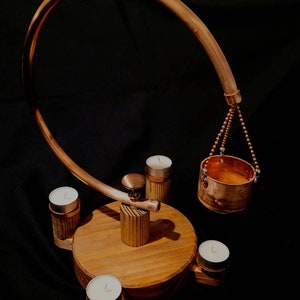 May include: A copper candle holder with a curved arm suspending a small bucket. The base is wooden, with several small candles in copper holders. The design is modern and decorative, suitable for home decor.