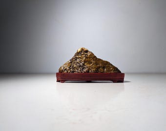 May include: A golden brown rock formation on a dark red wooden base. The rock is shaped like a mountain and has a rough, textured surface.