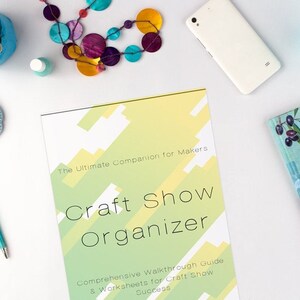 May include: A green and yellow guide titled "Craft Show Organizer: The Ultimate Companion for Makers" with the text "Comprehensive Walkthrough Guide & Worksheets for Craft Show Success".
