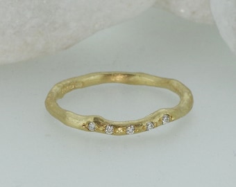 May include: A thin gold band ring with a textured surface and five small diamonds set in a row.