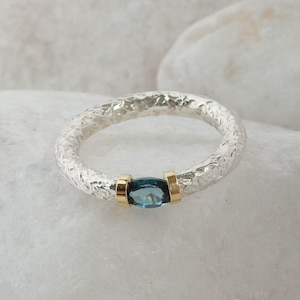 Puede incluir: Un anillo de plata con una banda texturizada y una piedra preciosa azul engastada en oro.