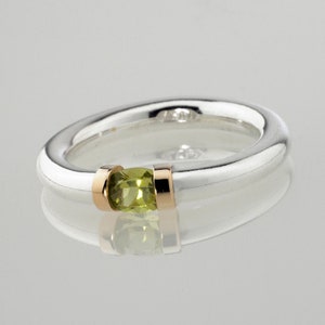 May include: A silver ring with a green gemstone set in a gold band.