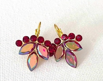 May include: A pair of gold-tone earrings featuring a cluster of round, deep red crystals along the top edge and marquise-shaped, iridescent crystals with pink and purple hues arranged in a leaf-like pattern at the bottom with lever-back closures.