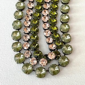 May include: A multi-strand necklace featuring round faceted crystals in alternating olive green and pale blush pink hues. Each individual crystal is set within a metallic prong setting, connected by thin metal links to form a layered chain design.