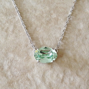 May include: A silver chain necklace with a light green oval-shaped gemstone pendant.