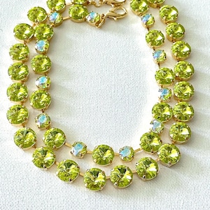 May include: A double-strand necklace featuring round, lime green faceted crystals set in gold-toned metal settings. The design includes smaller iridescent accent stones interspersed between the larger green crystals and a gold-toned chain extender.