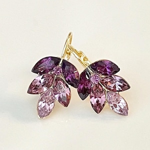 May include: A pair of dangle earrings with a cluster of purple and pink marquise-shaped crystals. The earrings have a gold-tone finish.