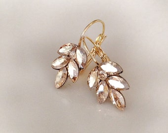 May include: A pair of gold hoop earrings with a cluster of clear crystal stones in the shape of leaves.
