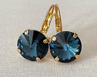 May include: A pair of gold hoop earrings with a dark blue round crystal in the center of each earring.