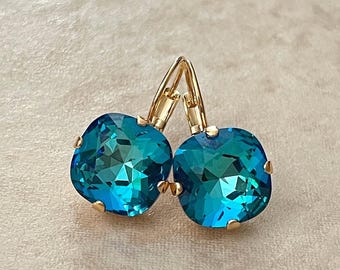 May include: A pair of gold earrings with teal blue square-shaped crystal stones.