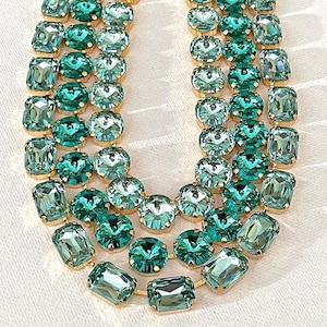 May include: Close-up of a necklace with multiple strands of teal-colored, faceted gemstones. The gemstones are set in gold-colored metal and arranged in rows. The necklace is displayed on a white surface.