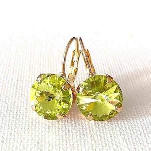 May include: A pair of round, faceted lime green crystal earrings set in gold-toned metal. Each earring features a circular stone with multiple facets that catch the light, secured by four prongs and attached to a gold-toned leverback closure mechanism.
