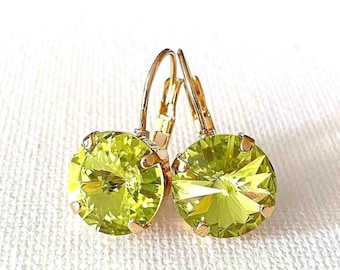 May include: A pair of round, faceted lime green crystal earrings set in gold-toned metal. Each earring features a circular stone with multiple facets that catch the light, secured by four prongs and attached to a gold-toned leverback closure mechanism.