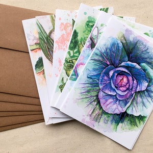 May include: A set of six blank greeting cards featuring watercolor illustrations of various vegetables. The cards are printed on white cardstock and come with brown envelopes.