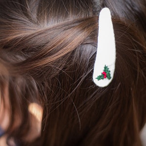 Pu&ograve; includere: Fermaglio per capelli bianco con un piccolo disegno di agrifoglio ricamato con foglie verdi e bacche rosse.