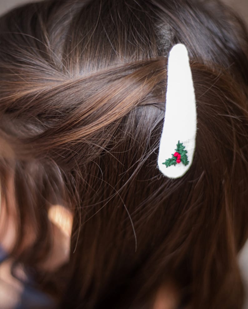 Pu&ograve; includere: Fermaglio per capelli bianco con un piccolo disegno di agrifoglio ricamato con foglie verdi e bacche rosse.