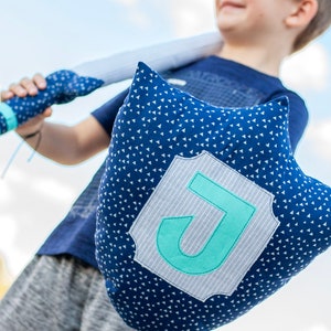 May include: A blue pillow with white triangle pattern and a gray and white patch with a turquoise letter J in the center.