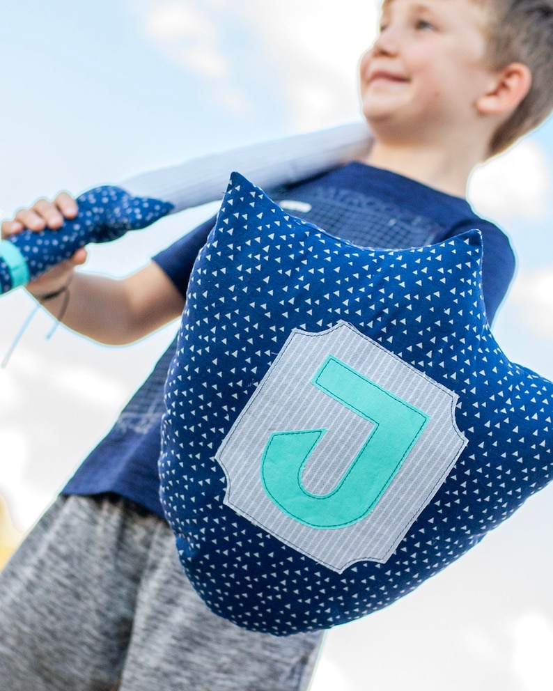 May include: A blue pillow with white triangle pattern and a gray and white patch with a turquoise letter J in the center.