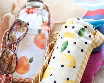 May include: Two fabric water bottle carriers with adjustable straps. One carrier is peach-colored with a gingham trim and the other is yellow with black polka dots and a gingham trim.