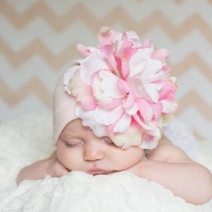 May include: A pink baby hat with a large pink and white flower on top. The hat is made of soft fabric and is perfect for a newborn baby.