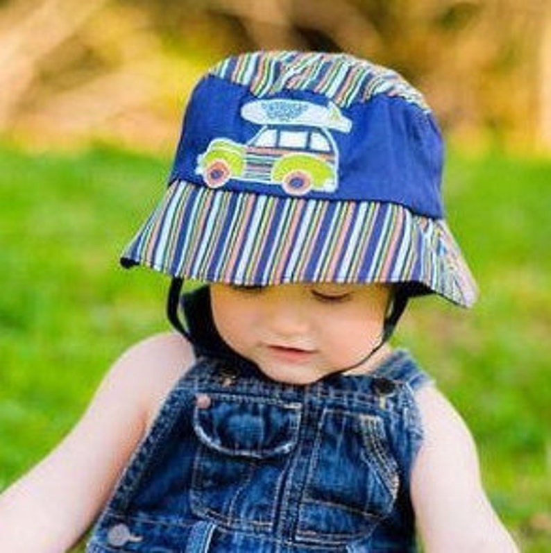May include: A blue and green striped bucket hat with a car and surfboard applique. The hat has a chin strap.