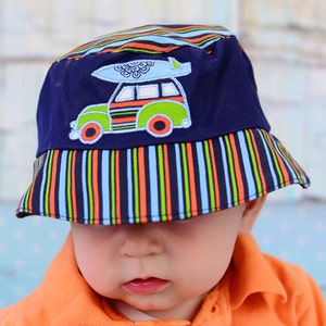 May include: A blue and white striped bucket hat with a colourful cartoon car and surfboard design. The hat is worn by a child wearing orange clothing.