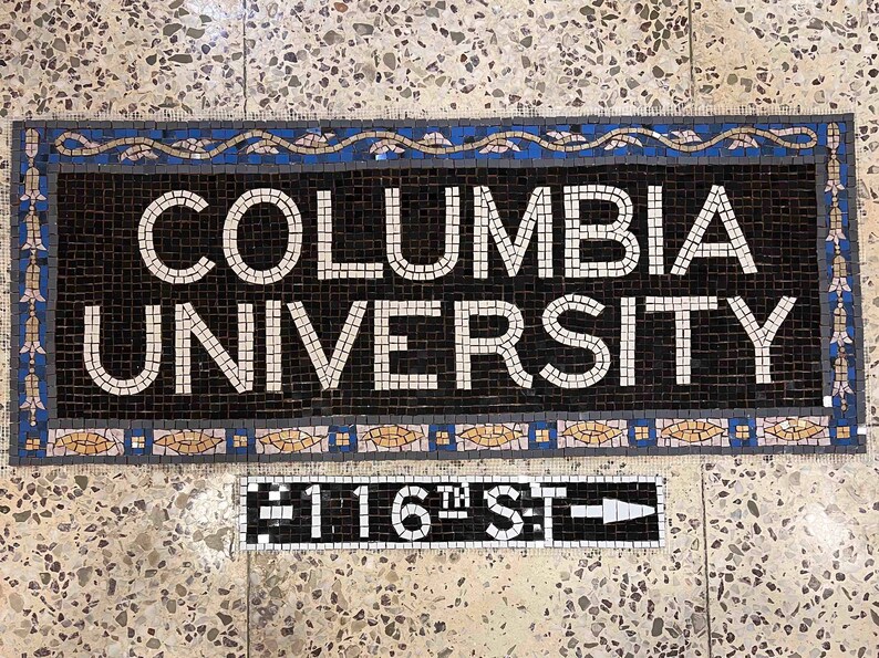 May include: A black and white mosaic tile sign that reads "COLUMBIA UNIVERSITY" with a blue and gold border. Below the sign is a black and white mosaic tile sign that reads "116TH ST" with a white arrow pointing to the right.