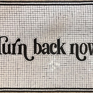 Op de afbeelding: Een zwart-witte mozaïekvloer met de woorden "Turn back now" in zwarte letters.