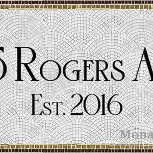 以下が含まれることがあります： 「115 Rogers Ave Est. 2016」の文字が入った長方形のモザイクの家の番号看板。扇形の模様の白い背景と金と茶色の縁があります。Mona Mosaic製です。