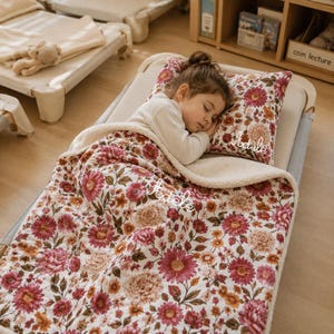 Peut inclure: Une couverture et un oreiller assorti à motif floral sur fond crème avec des fleurs roses, rouges et orange et des feuilles vertes. Le prénom Adele est brodé en écriture cursive blanche sur la couverture et sur l'oreiller.