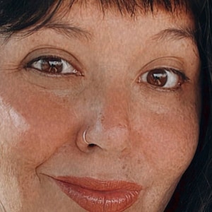 May include: A woman with long dark hair and a green and brown camouflage scarf. She is wearing a silver nose ring and a silver earring.