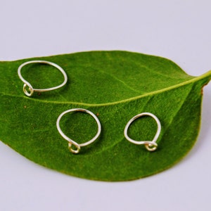 May include: Three silver rings with a twisted knot design are displayed on a green leaf.