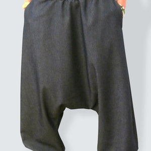 May include: Dark denim harem pants with a wide, dark brown waistband. The pants have deep pockets and are paired with striped sneakers with red laces. The style is casual and comfortable.