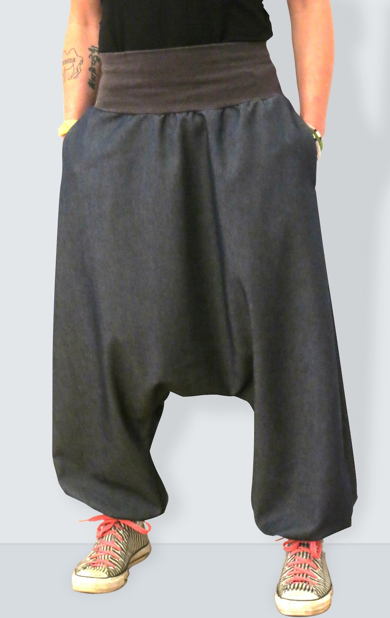 May include: Dark denim harem pants with a wide, dark brown waistband. The pants have deep pockets and are paired with striped sneakers with red laces. The style is casual and comfortable.