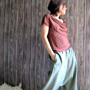 May include: A person wearing a brown knit hat, a brown draped-neck top, and light green harem pants. The pants have pockets and a blue waistband. The outfit is casual and comfortable.