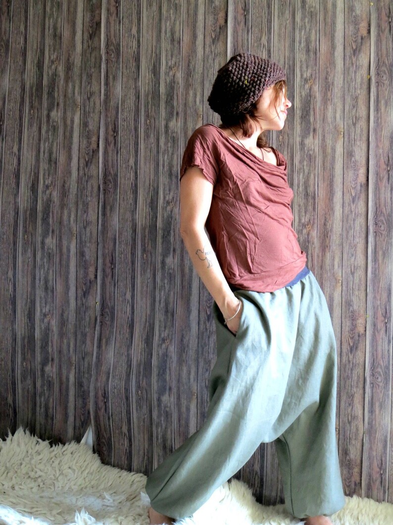 May include: A person wearing a brown knit hat, a brown draped-neck top, and light green harem pants. The pants have pockets and a blue waistband. The outfit is casual and comfortable.