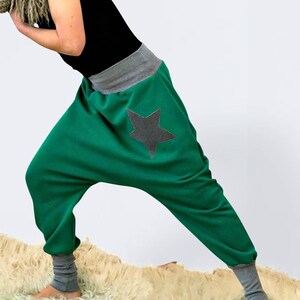 May include: Green, loose-fitting pants with a gray star patch on the back. The pants have a gray waistband and gray cuffs at the ankles.