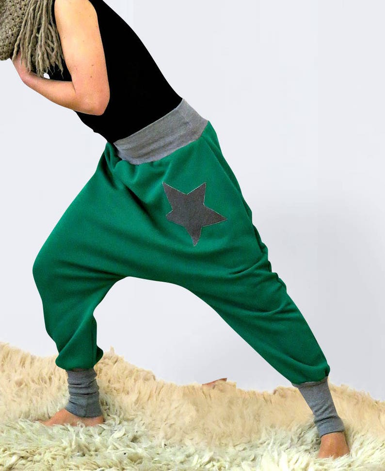 May include: Green, loose-fitting pants with a gray star patch on the back. The pants have a gray waistband and gray cuffs at the ankles.