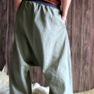 May include: Olive green harem pants with a black waistband. The pants have a loose, flowing design and are made of a lightweight fabric. The pants have pockets and are gathered at the ankles.