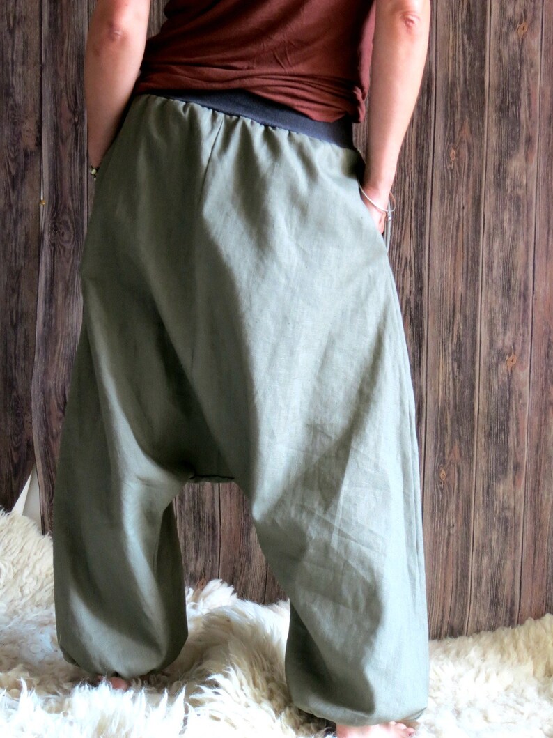 May include: Olive green harem pants with a black waistband. The pants have a loose, flowing design and are made of a lightweight fabric. The pants have pockets and are gathered at the ankles.