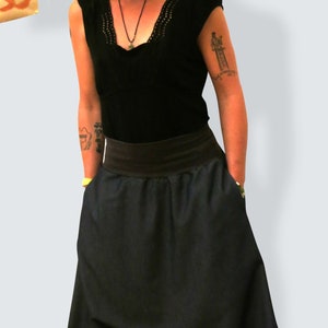 May include: A person wearing a coral-colored knit hat, a black top with a lace neckline, and dark blue harem pants. The pants have a wide waistband and pockets. The person is also wearing sneakers with red laces.