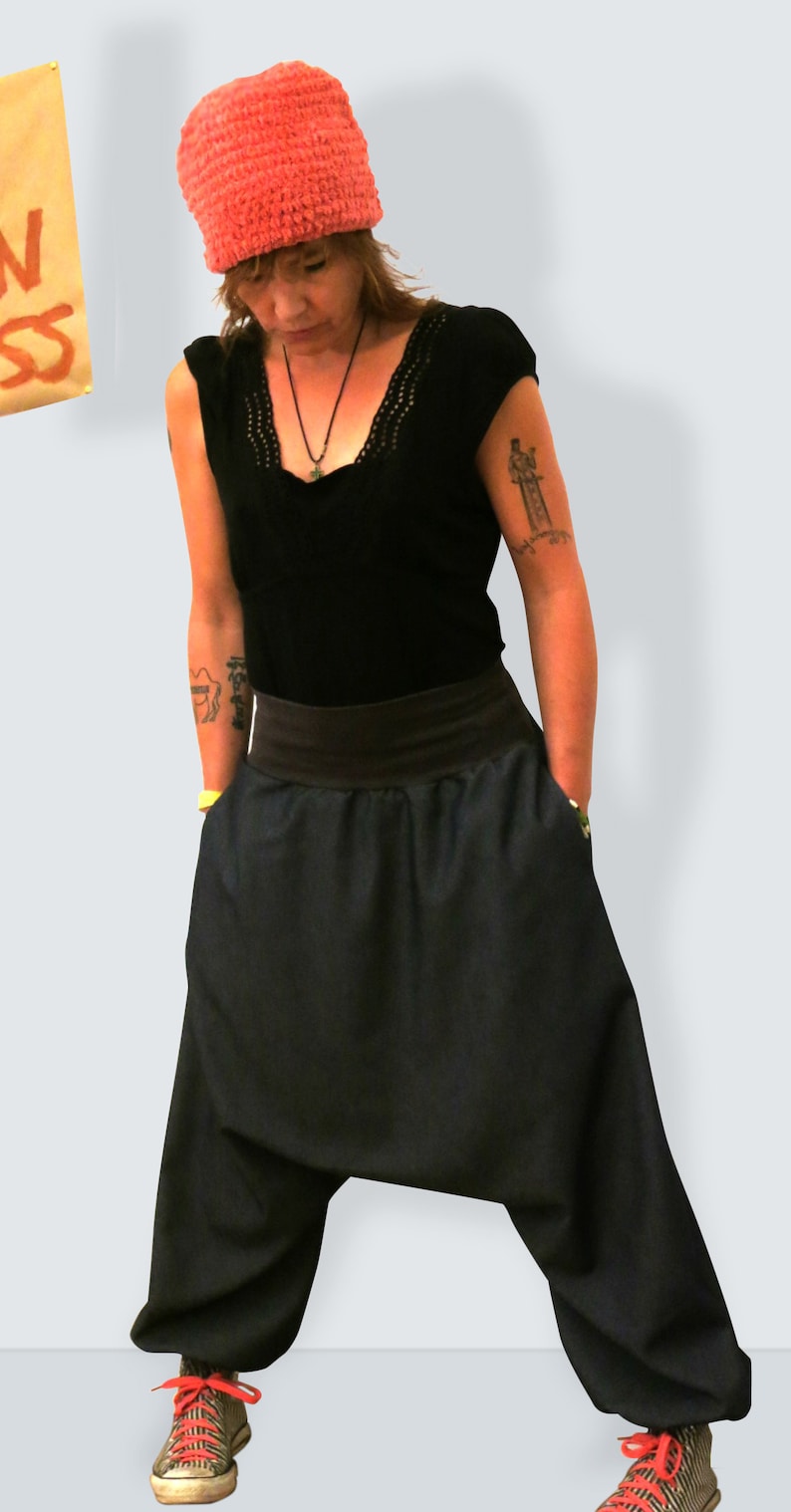 May include: A person wearing a coral-colored knit hat, a black top with a lace neckline, and dark blue harem pants. The pants have a wide waistband and pockets. The person is also wearing sneakers with red laces.