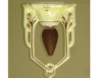 May include: A cream-colored ceramic shelf with gold accents and an ornate design. The shelf has a rounded top and a pointed bottom. It is designed to be mounted on a wall.