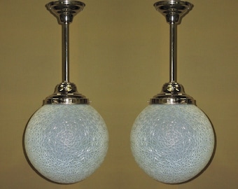 Op de afbeelding: Twee zilveren hanglampen met witte, gematteerde glazen bolvormige lampenkappen. De bollen hebben een geometrisch patroon.