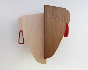 May include: A wooden wall sculpture with two red geometric shapes attached. The sculpture is made of two different types of wood, one light and one dark.