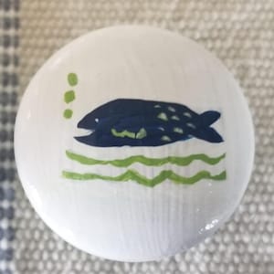 May include: A white ceramic knob with a blue fish and green waves painted on it.